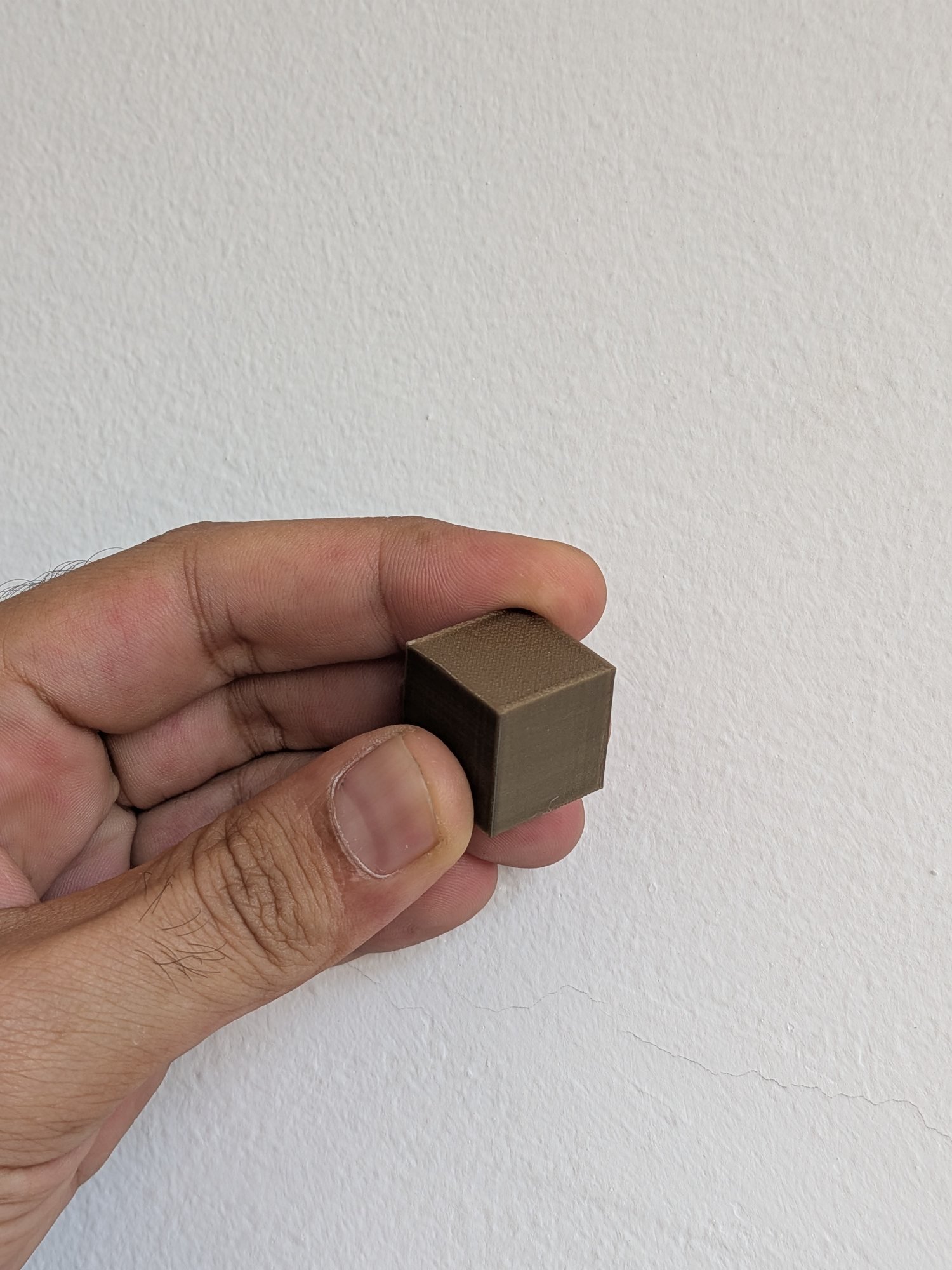 Cubetto di prova in filamento oro tenuto in mano, per vedere colore e finitura prima di stampare l'insegna